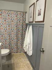 Full bathroom with wainscoting, toilet, tile patterned flooring, vanity, and a decorative wall