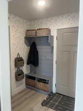 Mudroom with wood finished floors, a textured ceiling, baseboards, and wallpapered walls