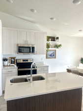 Kitchen featuring modern cabinets, appliances with stainless steel finishes, light wood-style floors, vaulted ceiling, and light stone countertops