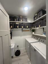 Clothes washing area with laundry area, washing machine and dryer, light wood finished floors, and a textured ceiling