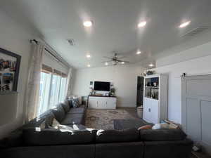 Living room with lofted ceiling, a barn door, visible vents, and ceiling fan