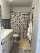 Full bath featuring toilet, a decorative wall, a wainscoted wall, wood finished floors, and vanity