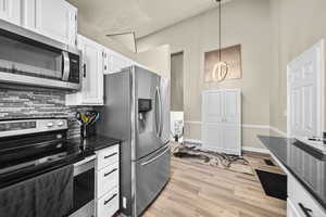 Kitchen featuring stainless steel appliances, tasteful backsplash, hanging light fixtures, white cabinets, and dark stone counters