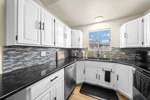 Kitchen with stainless steel dishwasher, white cabinetry, a sink, and stove