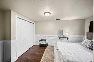 Bedroom with a wainscoted wall, dark wood finished floors, a closet, visible vents, and a textured ceiling