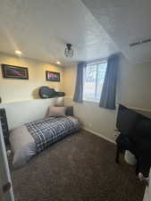 Bedroom with a textured ceiling, carpet, visible vents, and baseboards