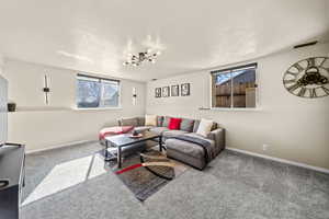 Carpeted living area with baseboards, a textured ceiling, visible vents, and a wealth of natural light