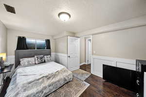 Bedroom featuring a textured ceiling, dark wood-type flooring, wainscoting, and visible vents