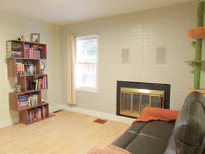 Living room with a brick fireplace, baseboards, visible vents, and wood finished floors