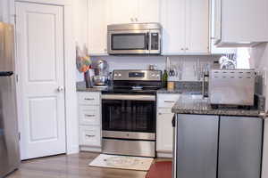 Kitchen featuring white cabinetry, appliances with stainless steel finishes, dark wood-style flooring, and granite countertops