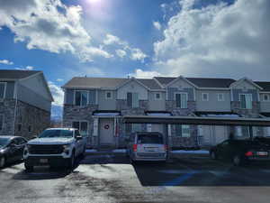 View of front facade with a residential view, stone siding, and covered and uncovered parking