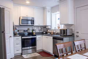 Kitchen with granite countertops, stainless steel appliances, a sink, and white cabinetry