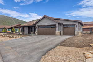 Single story home with stone siding, driveway, a garage, and a mountain view