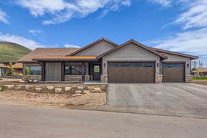 View of front of house featuring an attached garage, stone siding, and asphalt driveway