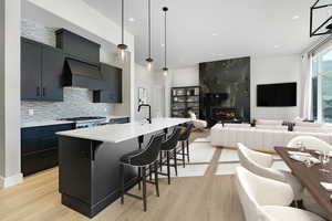Kitchen with dark cabinets, hanging light fixtures, a kitchen island with sink, a kitchen breakfast bar, and decorative backsplash