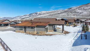 Snow covered rear of property with stone siding, a residential view, and a mountain view