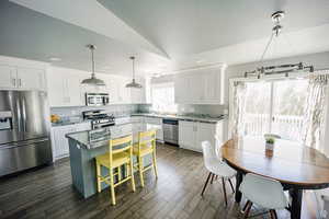 Kitchen featuring white cabinets, appliances with stainless steel finishes, a breakfast bar, light stone counters, and a center island