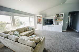 Carpeted living area featuring baseboards and vaulted ceiling