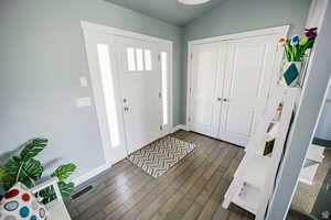 Entrance foyer featuring lofted ceiling, baseboards, visible vents, and dark wood-style flooring