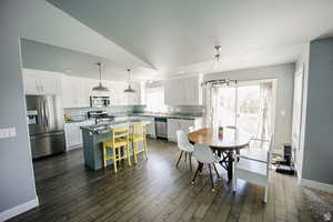 Kitchen featuring a breakfast bar, decorative light fixtures, appliances with stainless steel finishes, white cabinetry, and a kitchen island