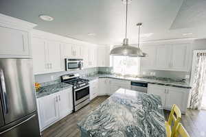 Kitchen with appliances with stainless steel finishes, white cabinets, and light stone countertops