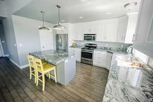 Kitchen with white cabinets, a kitchen island, appliances with stainless steel finishes, a breakfast bar area, and pendant lighting