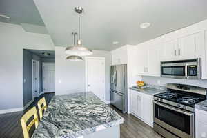 Kitchen featuring light stone countertops, white cabinetry, stainless steel appliances, and pendant lighting