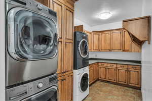 Clothes washing area featuring stacked washing maching and dryer and cabinet space