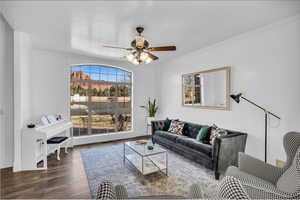 Living room with dark wood-style flooring, visible vents, a ceiling fan, baseboards, and ornamental molding