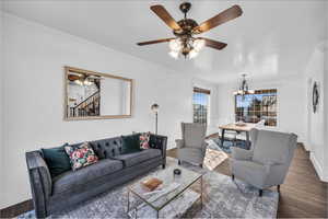 Living area with ceiling fan with notable chandelier, baseboards, ornamental molding, stairway, and dark wood-style floors