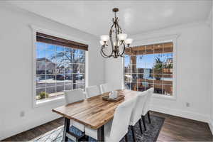 Dining area with ornamental molding, dark wood-type flooring, a notable chandelier, and baseboards