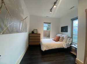 Bedroom featuring dark wood-type flooring, rail lighting, visible vents, and baseboards