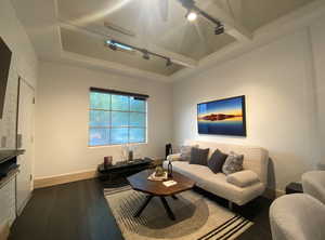 Living area with track lighting, a tray ceiling, dark wood-style flooring, and baseboards