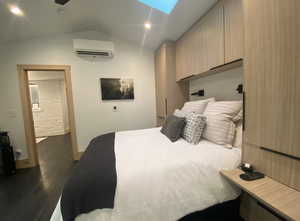 Bedroom featuring vaulted ceiling with skylight, baseboards, dark wood finished floors, and a wall mounted air conditioner