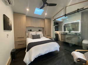 Bedroom with dark wood-style floors, recessed lighting, a ceiling fan, an AC wall unit, and vaulted ceiling with skylight