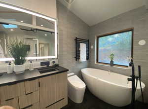 Bathroom featuring tile patterned flooring, vaulted ceiling, vanity, a freestanding tub, and tile walls