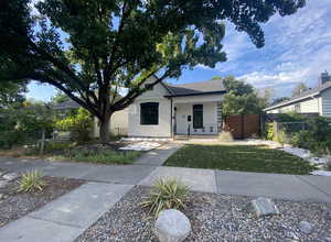 Bungalow-style house featuring a fenced front yard, covered porch, roof with shingles, stucco siding, and a front lawn