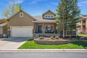 View of front of property with covered porch, stone siding, stucco siding, and driveway