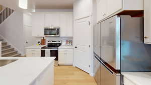 Kitchen featuring decorative backsplash, appliances with stainless steel finishes, white cabinetry, light stone countertops, and light wood-type flooring