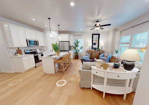 Kitchen featuring a kitchen island with sink, stainless steel appliances, open floor plan, light countertops, and decorative light fixtures