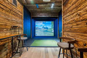 Recreation room with golf simulator, wood walls, wooden ceiling, and wood finished floors