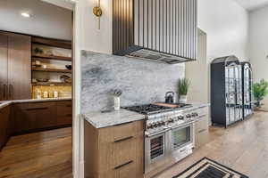 Kitchen featuring wall chimney exhaust hood, light wood-style flooring, light countertops, double oven range, and open shelves