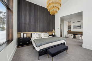 Bedroom with carpet floors, a lit fireplace, baseboards, and a notable chandelier