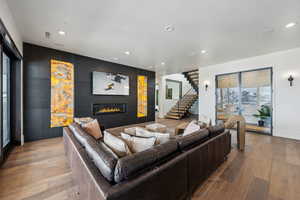 Living room featuring stairs, light wood finished floors, a glass covered fireplace, and recessed lighting