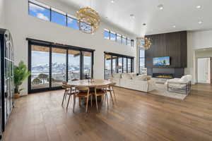 Dining room featuring recessed lighting, a notable chandelier, a fireplace, wood finished floors, and a towering ceiling