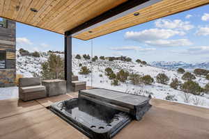 Snow covered patio featuring a mountain view and a hot tub