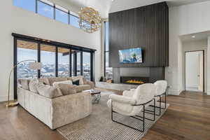 Living area with a warm lit fireplace, plenty of natural light, wood finished floors, and an inviting chandelier