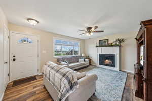 Living room with a warm lit fireplace, dark wood finished floors, and baseboards