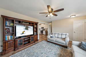 Living room with ceiling fan, baseboards, and dark wood-style flooring