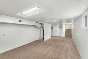 Below grade area with a textured ceiling, stairway, carpet, and visible vents